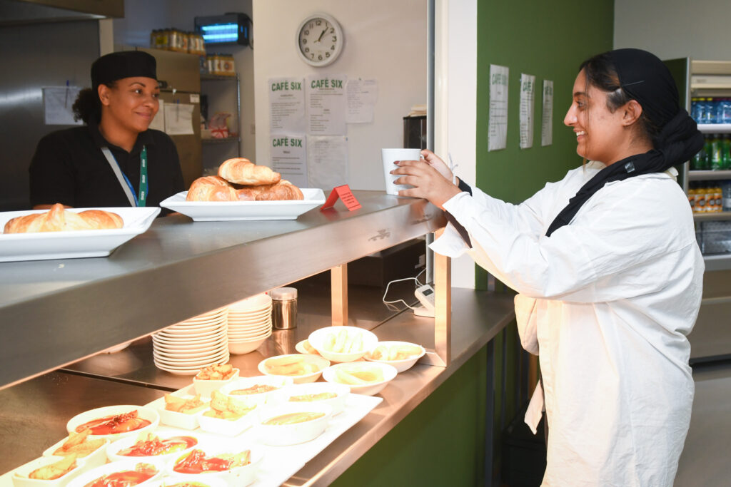 a picture of a student taking food from the dinner hall with a dinner lady smiling at them