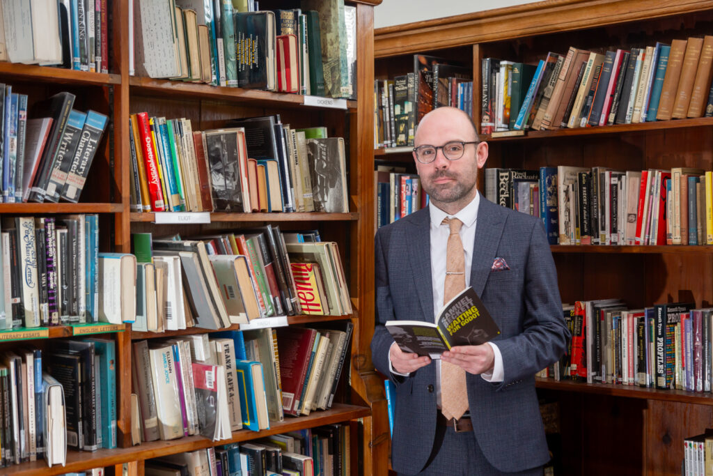 An image of Head of English, Mr Kenndey, standing in the library with a book.