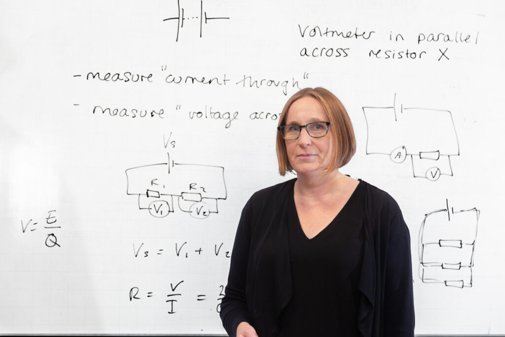 An image of Head of Physics, Dr Hudgson, standing in front of a physics whiteboard.