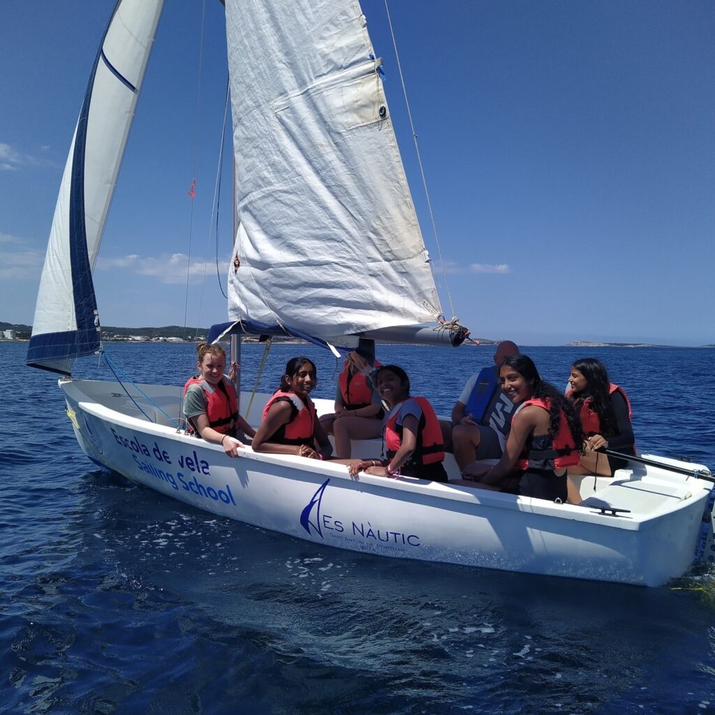 Pupils in a small sailing boat off the coast of Ibiza. Blue sky, blue sea and a white boat with white sails.
