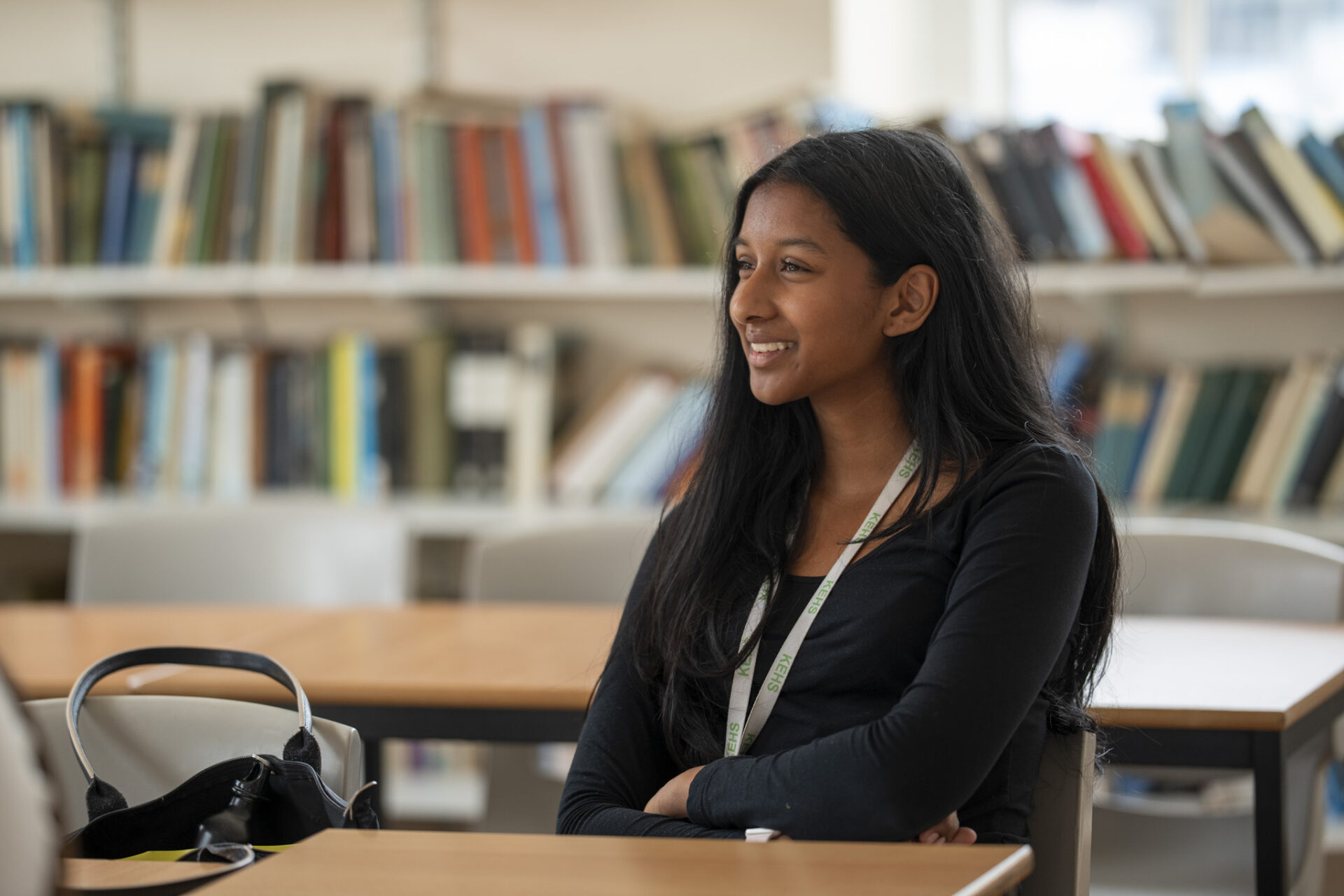 A young girl sits at a desk in front of bookshelves.