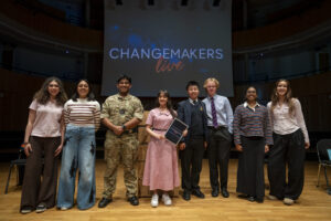 Eight pupils stand on a stage in front of a screen that reads "CHANGEMAKERS live".
