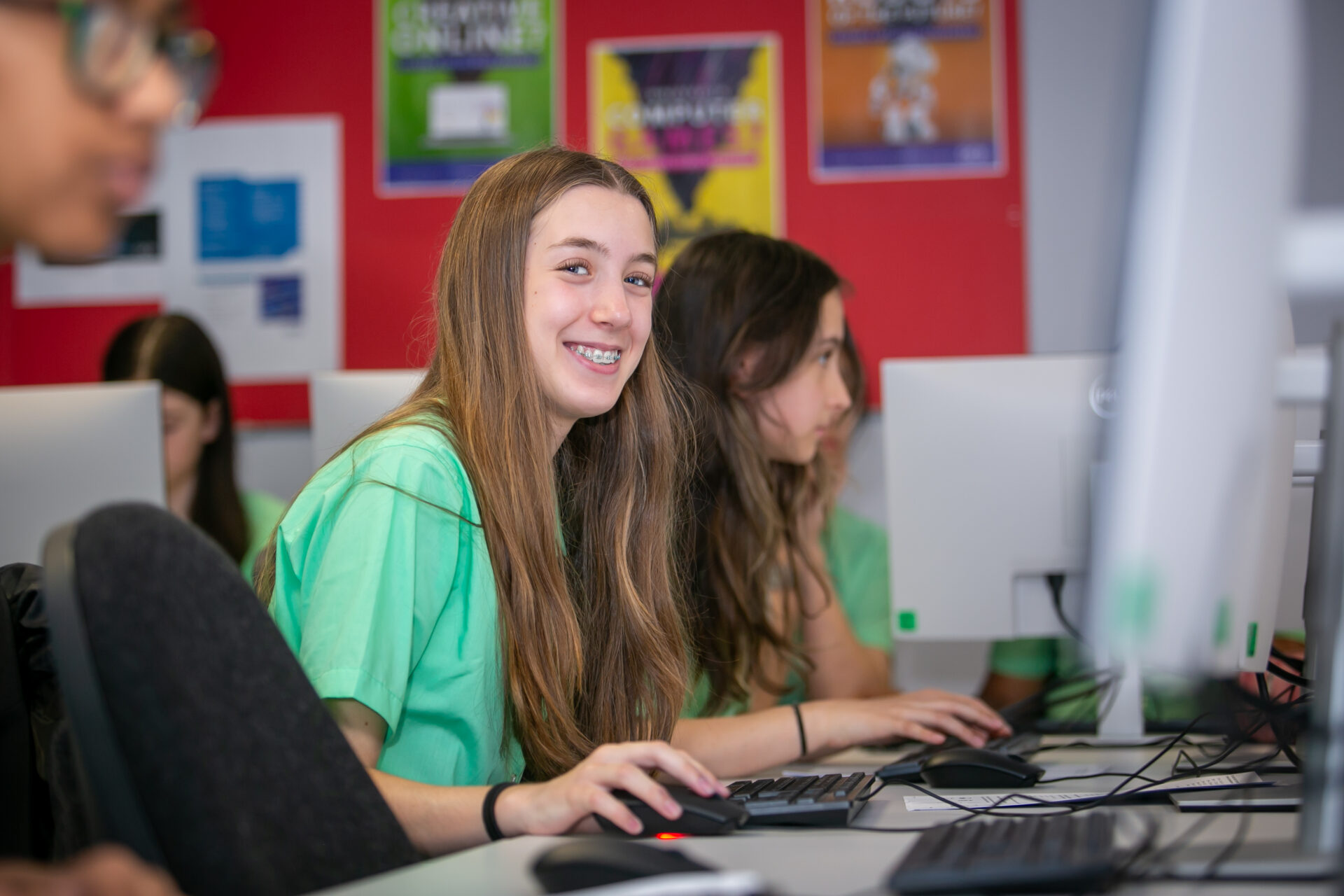 A smiling student looking at the camera while working on a computer in a classroom.
