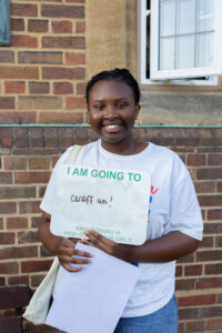 Smiling student standing by a building holding a white poster that reads “I AM GOING TO” and “Cardiff uni,”