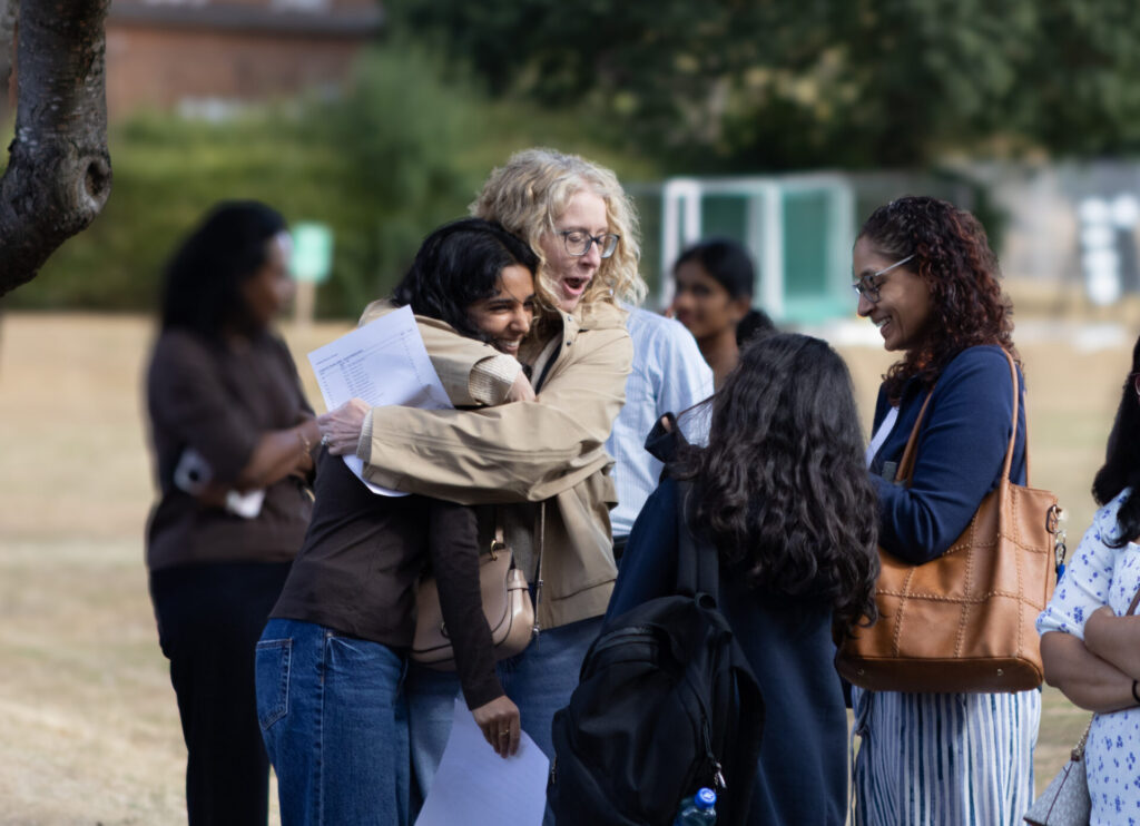 A group of people outdoors happy and smiling reading their exam results, with two people embracing.