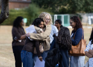 A group of people outdoors happy and smiling reading their exam results, with two people embracing.