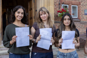 Three students stand outside a school and smiling while holding exam results.
