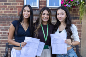Three people smiling and posing outside school - two of the people are holding exam results.