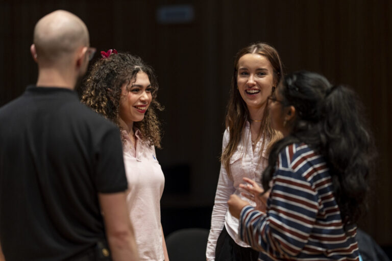 Four people chatting in a theatre or conference setting.